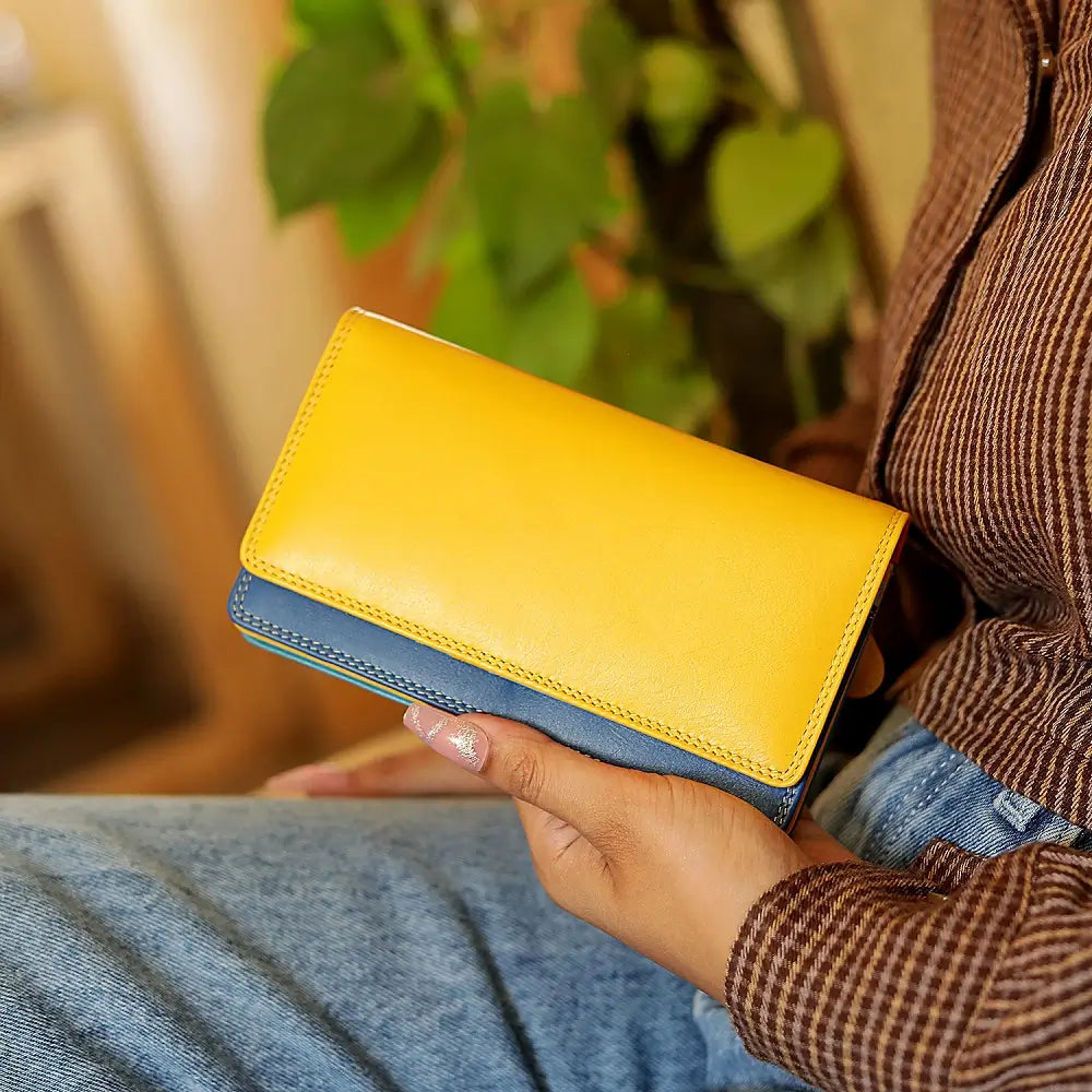 Person holding a yellow  wallet with a blurred indoor background