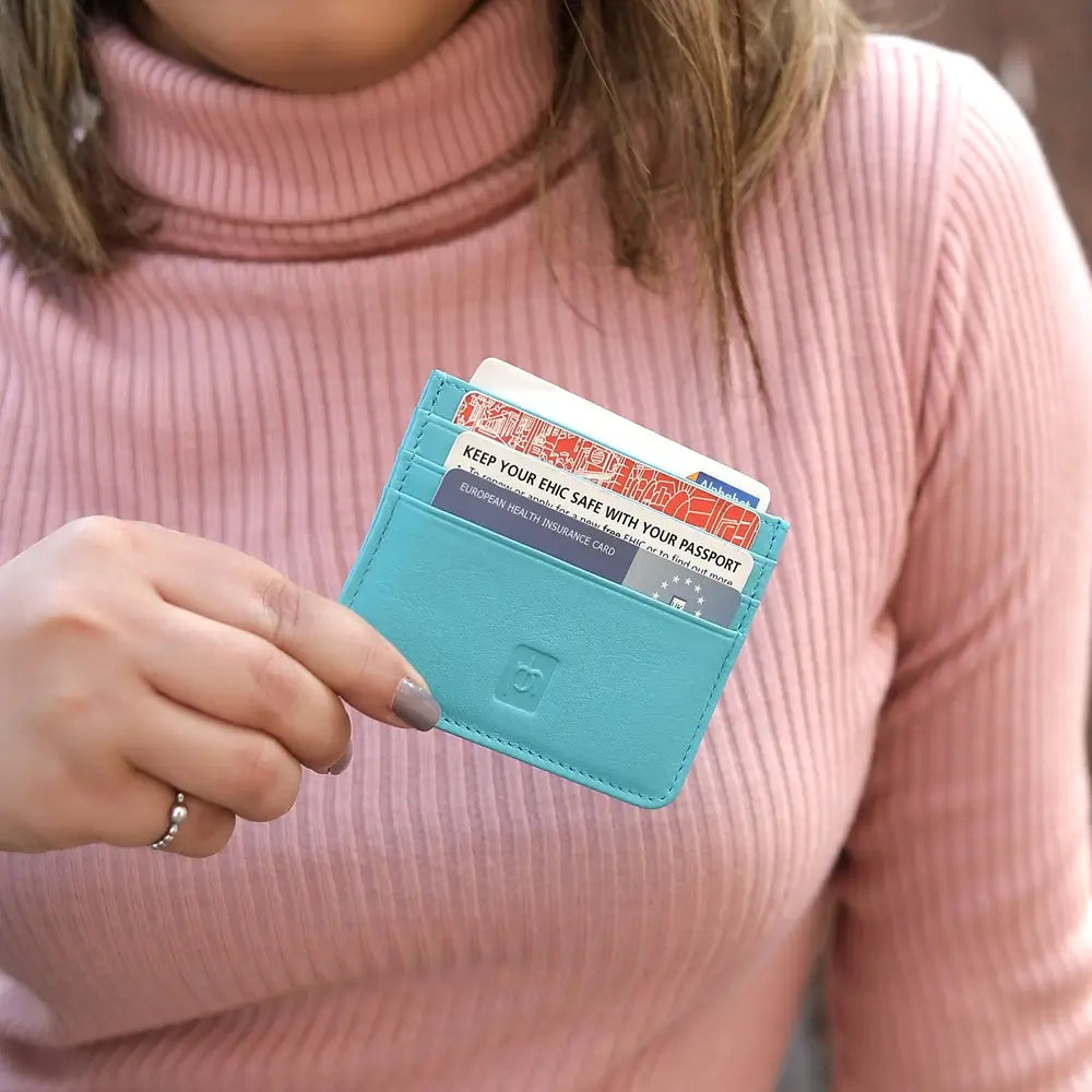 A close-up of a person wearing a pink ribbed turtleneck sweater and holding a turqoise leather card holder wallet containing credit cards.