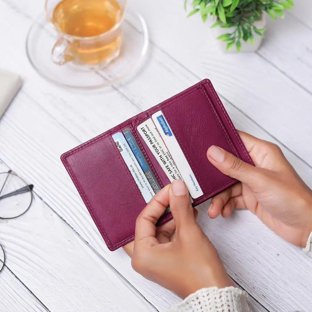 Person holding a fuchsia wallet with cards on a desk with a cup of coffee.