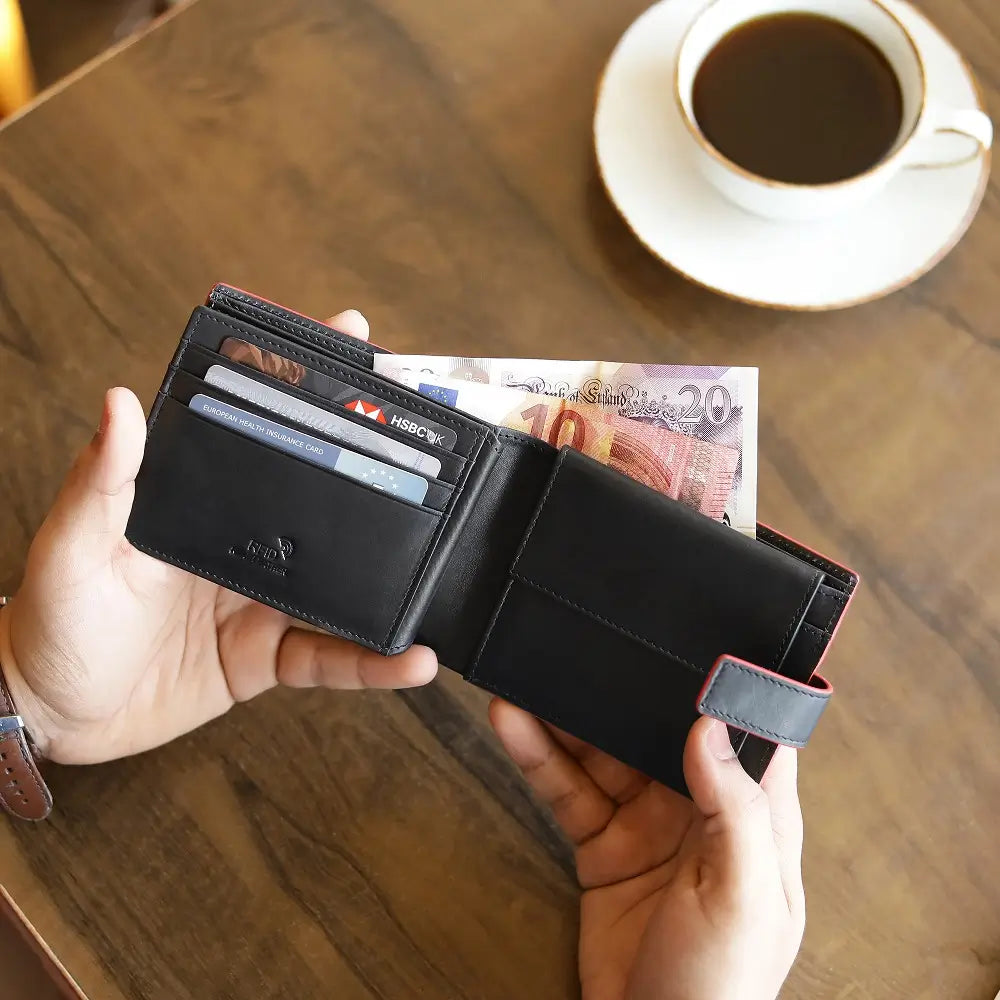 Person holding a black wallet with cards and money on a wooden table with a cup of coffee.