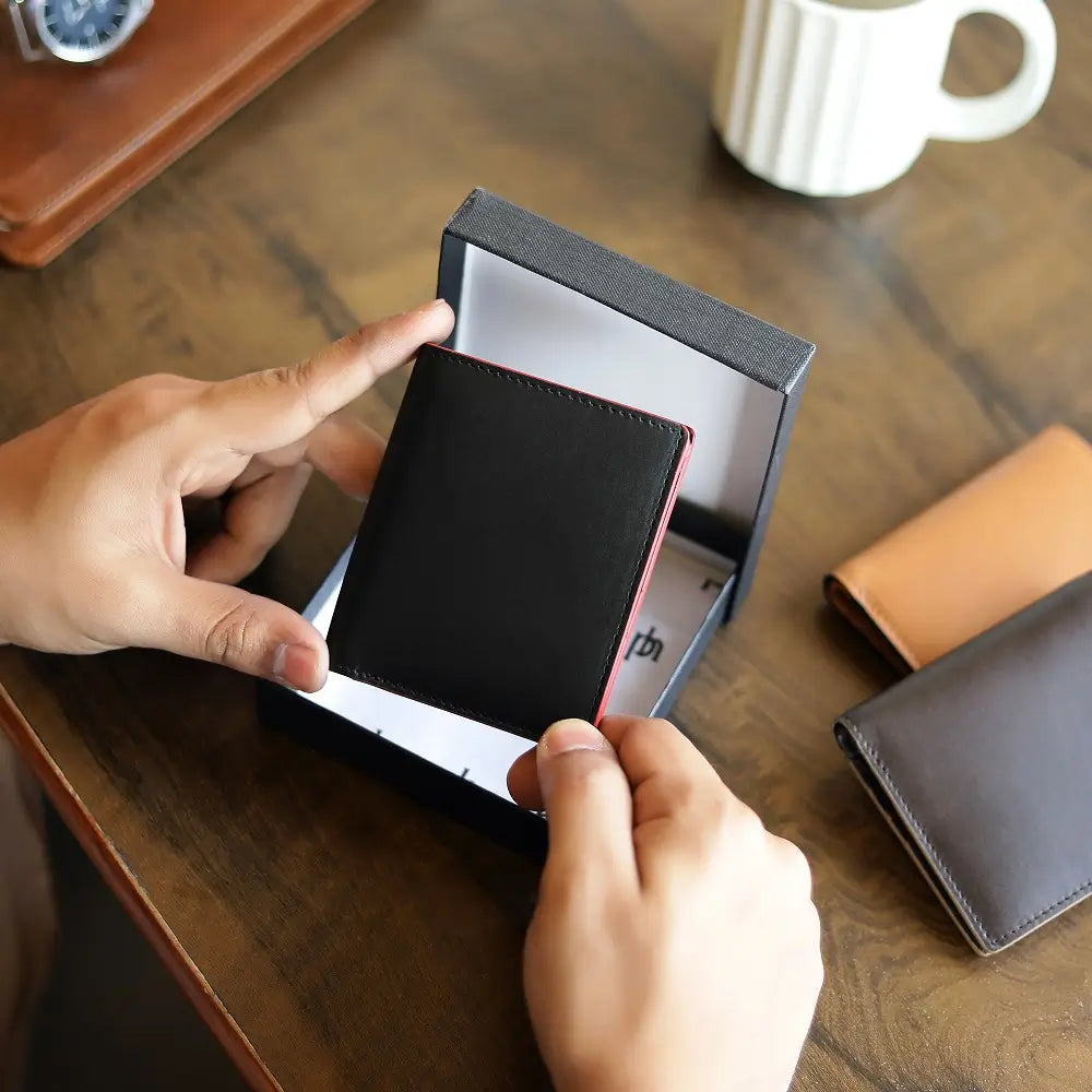 Person opening a black wallet with a red interior on a wooden table.