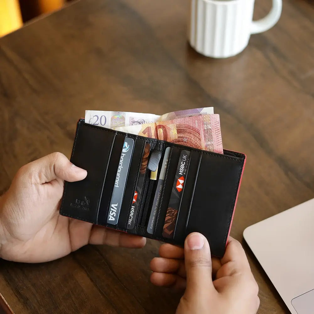 Person holding a black wallet with money and cards on a wooden table.
