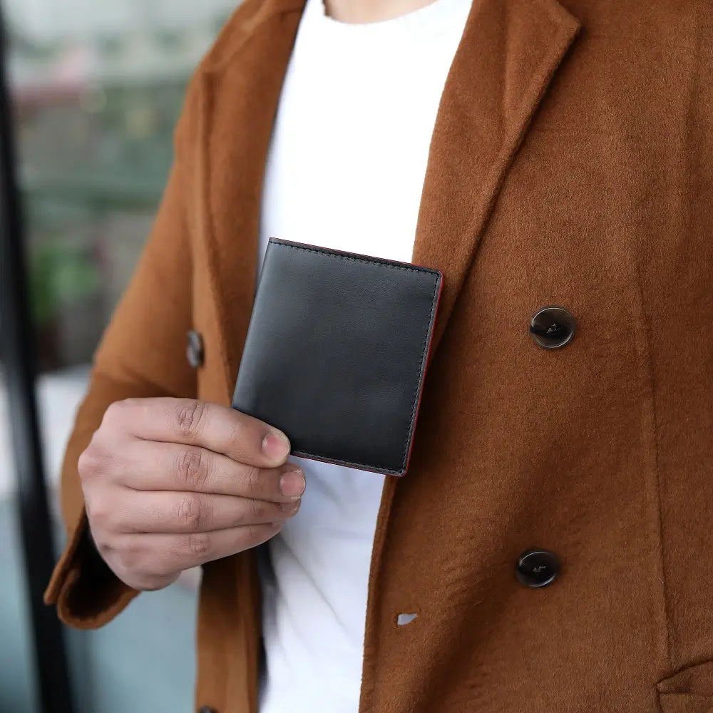 Person wearing a brown coat holding a black wallet.