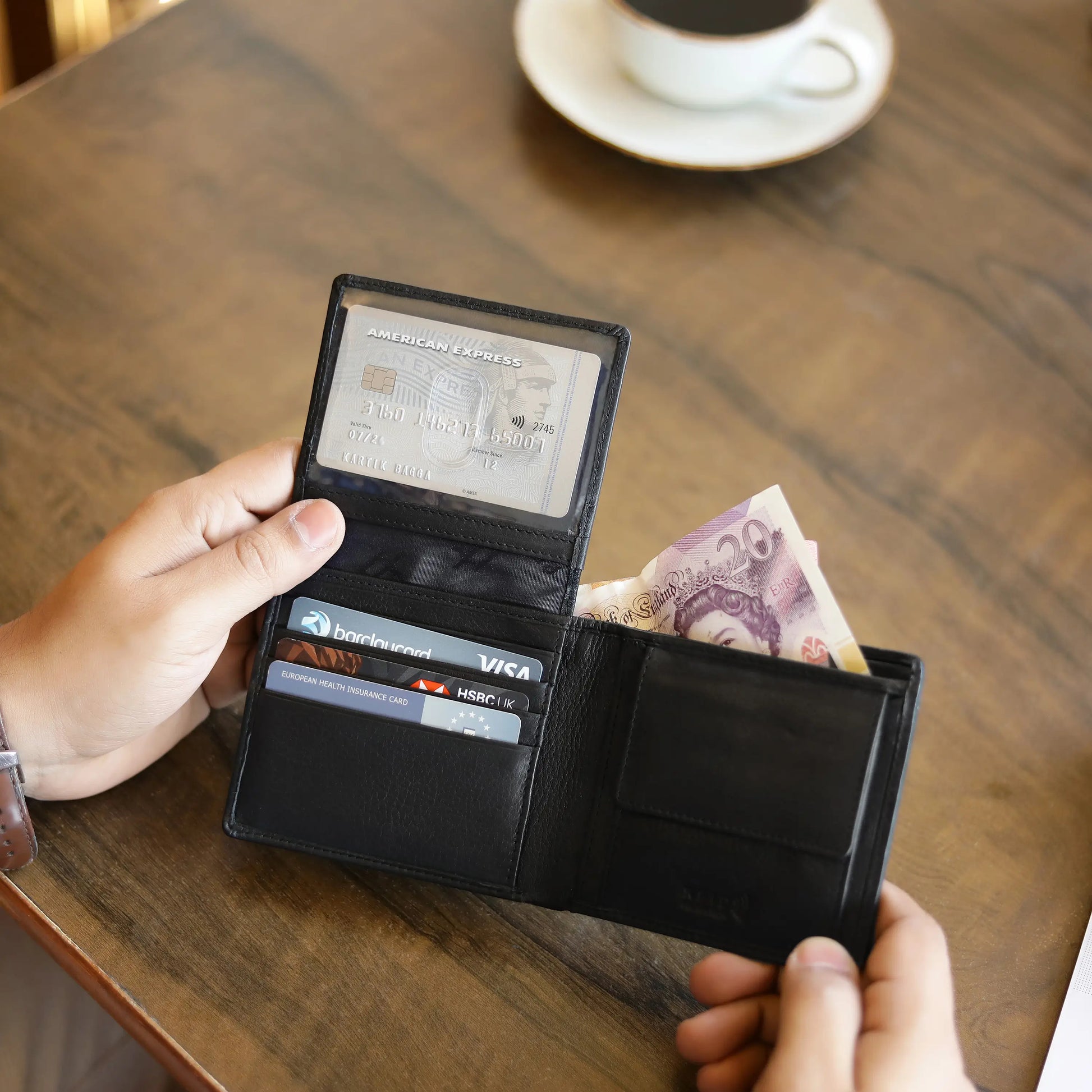 Person holding an open black wallet with cards and money on a wooden table.