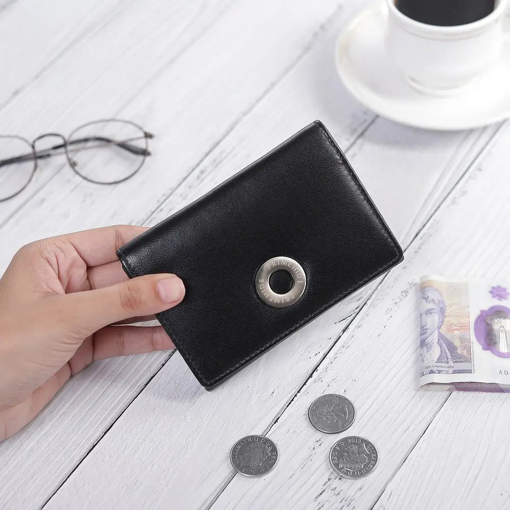 Black wallet held by a hand on a white wooden surface with coins and a cup of coffee.