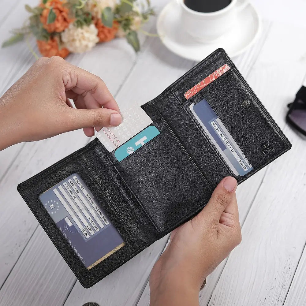 Black wallet with cards held open by a hand on a light wooden surface.