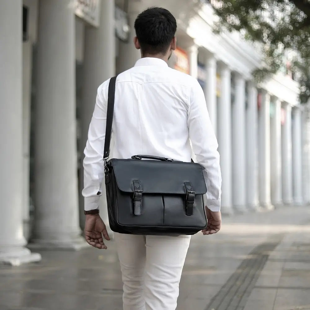 Man in white shirt and pants carrying a black leather laptop bag on a city street.