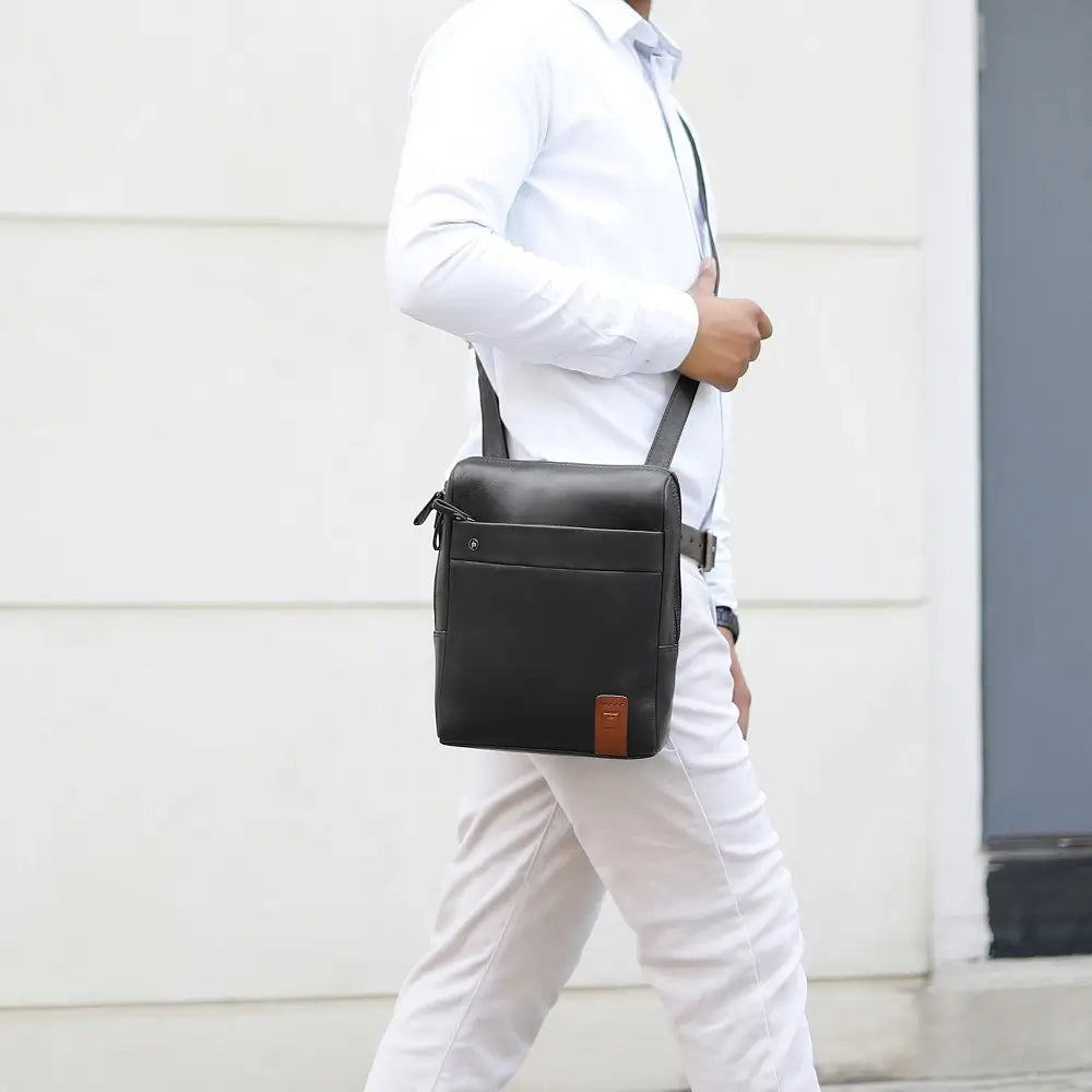 Person wearing a black messenger 
 bag in front of a light-colored wall.