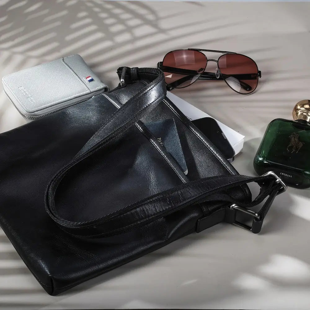 Black leather bag with sunglasses and a phone on a light surface