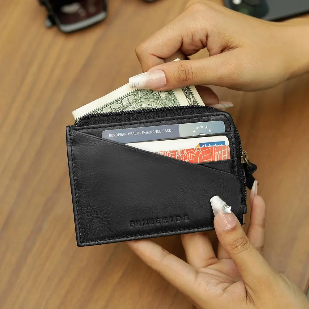 Person holding a black wallet with cards and money on a wooden surface
