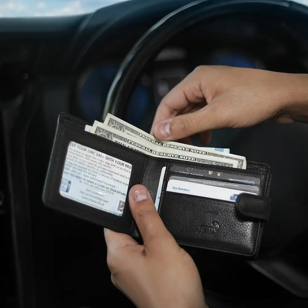 Person holding a black wallet with money and cards inside, sitting in a car.