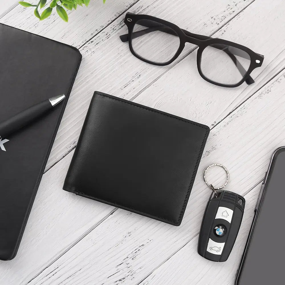 Black leather wallet, glasses, pen, phone, and car key fob on a white wooden surface.