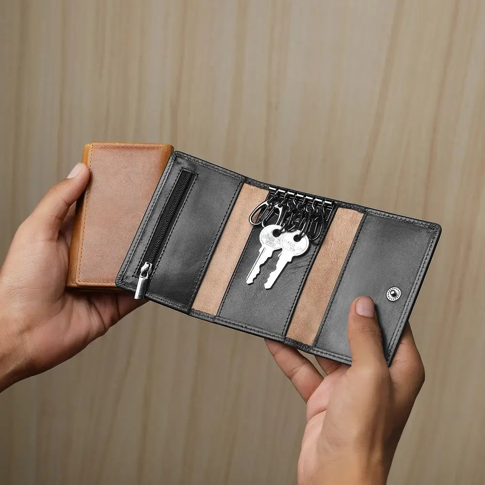 Person holding black leather key holder against  a grey background