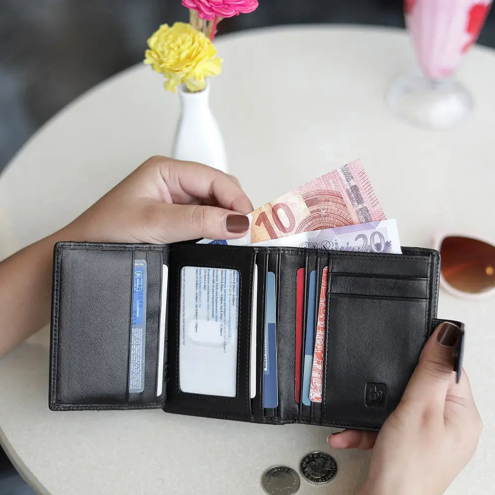 Person holding soft black leather trifold purse with secure tab fastening