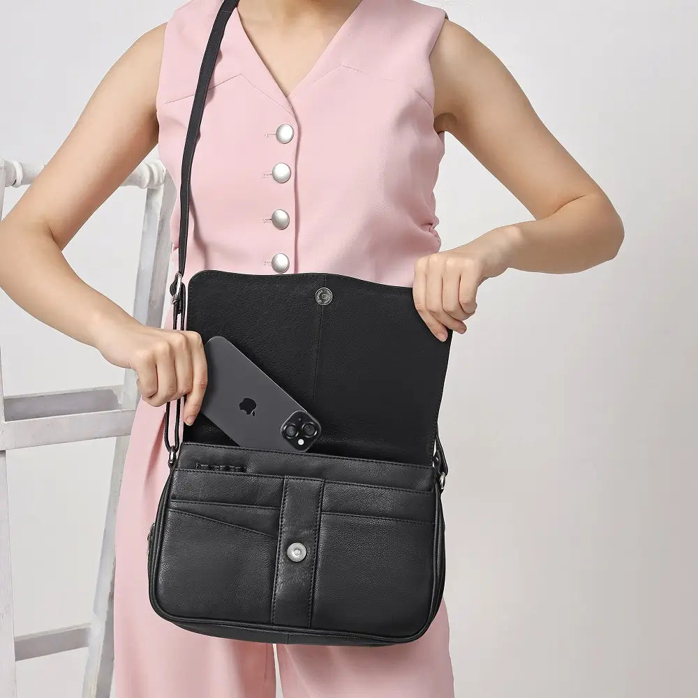 Person wearing a pink sleeveless top and holding a black handbag against a plain background
