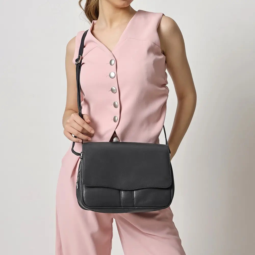 Person wearing a pink sleeveless top and holding a black handbag against a plain background