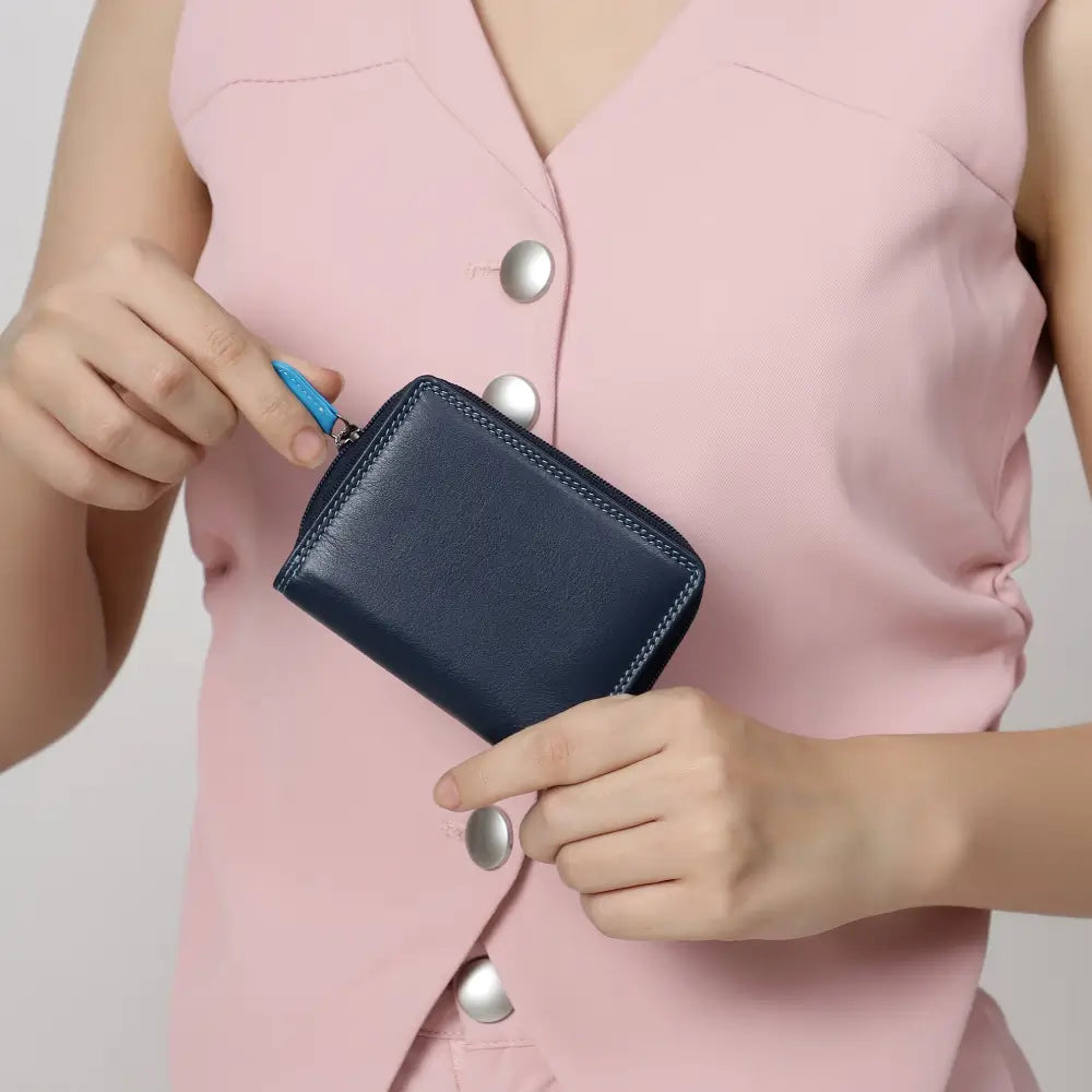 Person holding a blue wallet against a light pink background