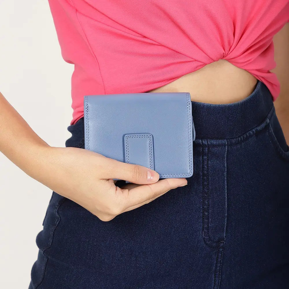Person holding a blue wallet with a pink top and dark jeans against a light background
