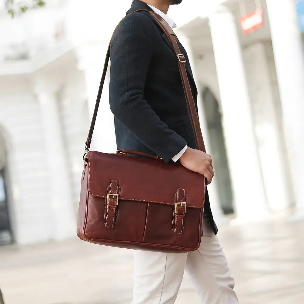 Person carrying a brown leather satchel bag outdoors