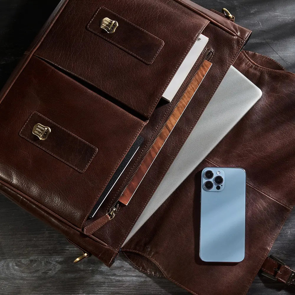 Brown leather laptop bag with laptop and phone on a wooden surface