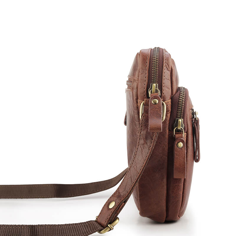 Brown leather crossbody bag with gold zippers on a white background