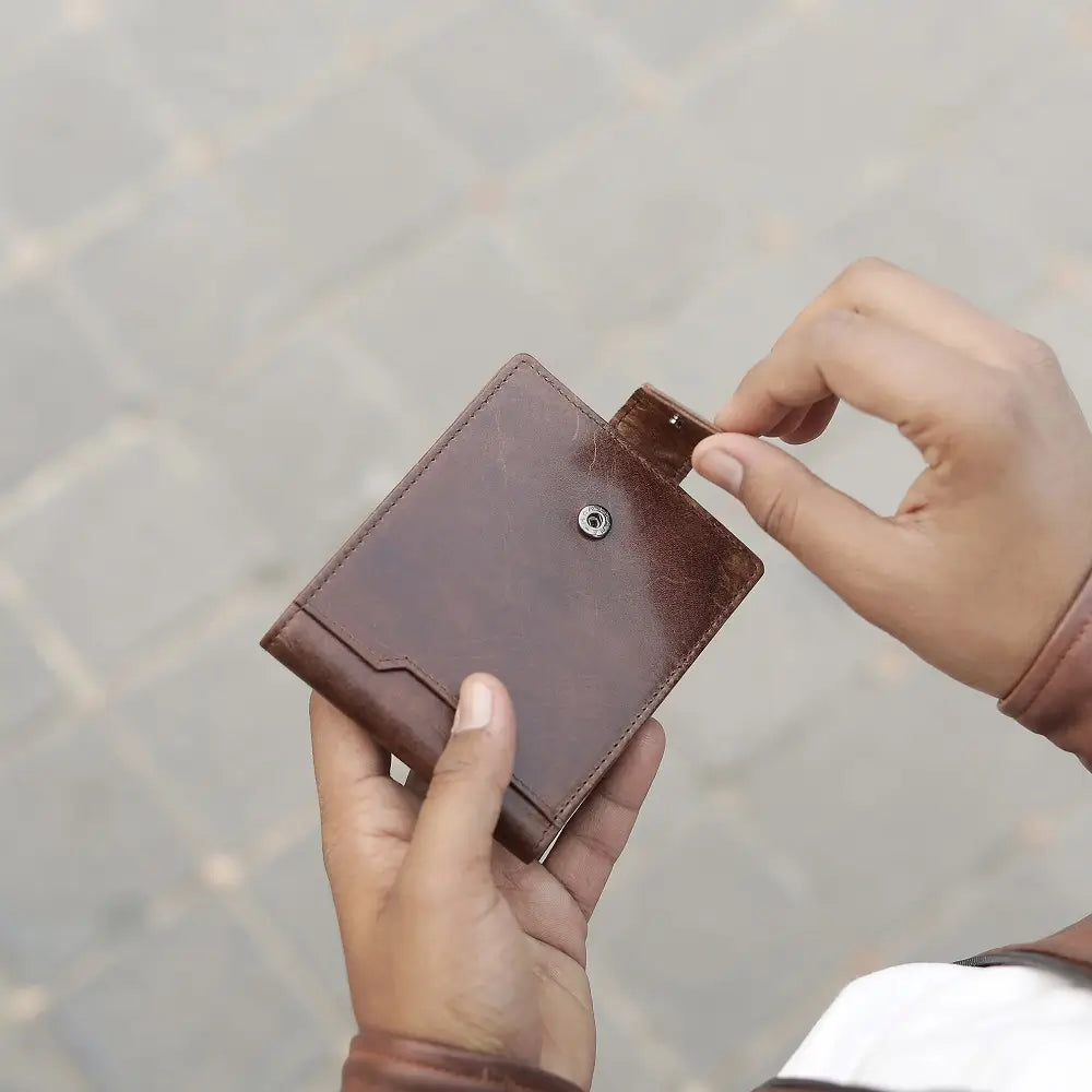 Brown leather trifold  wallet held by a person against a blurred background