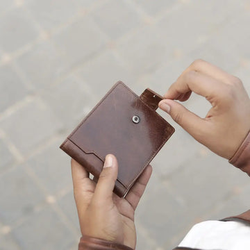 Brown leather trifold  wallet held by a person against a blurred background