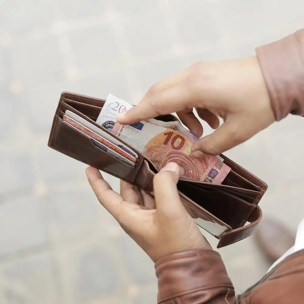 Person holding a brown wallet with money against a blurred background