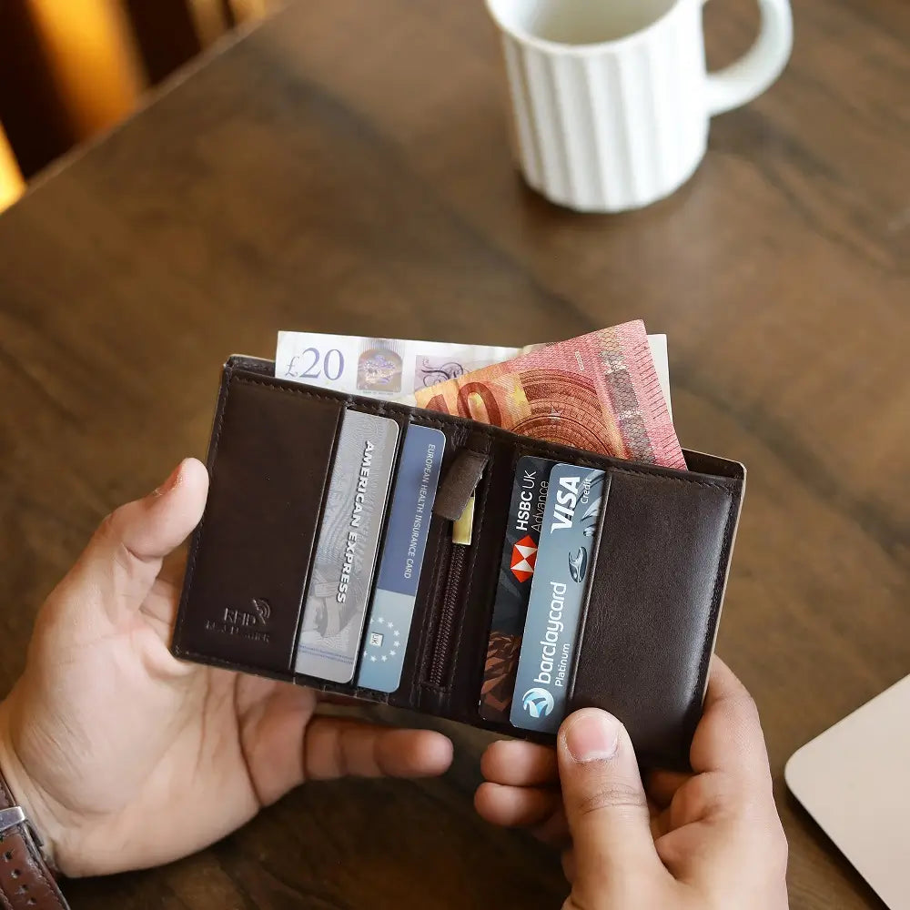Person holding a wallet with money and cards on a wooden table