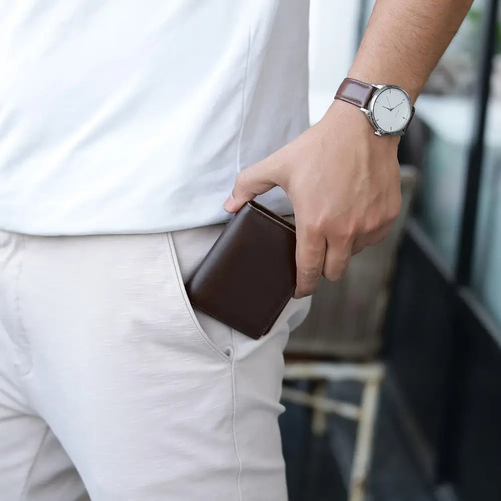 Person wearing a white shirt and light-colored pants, with a brown wallet in their pocket and a watch on their wrist.