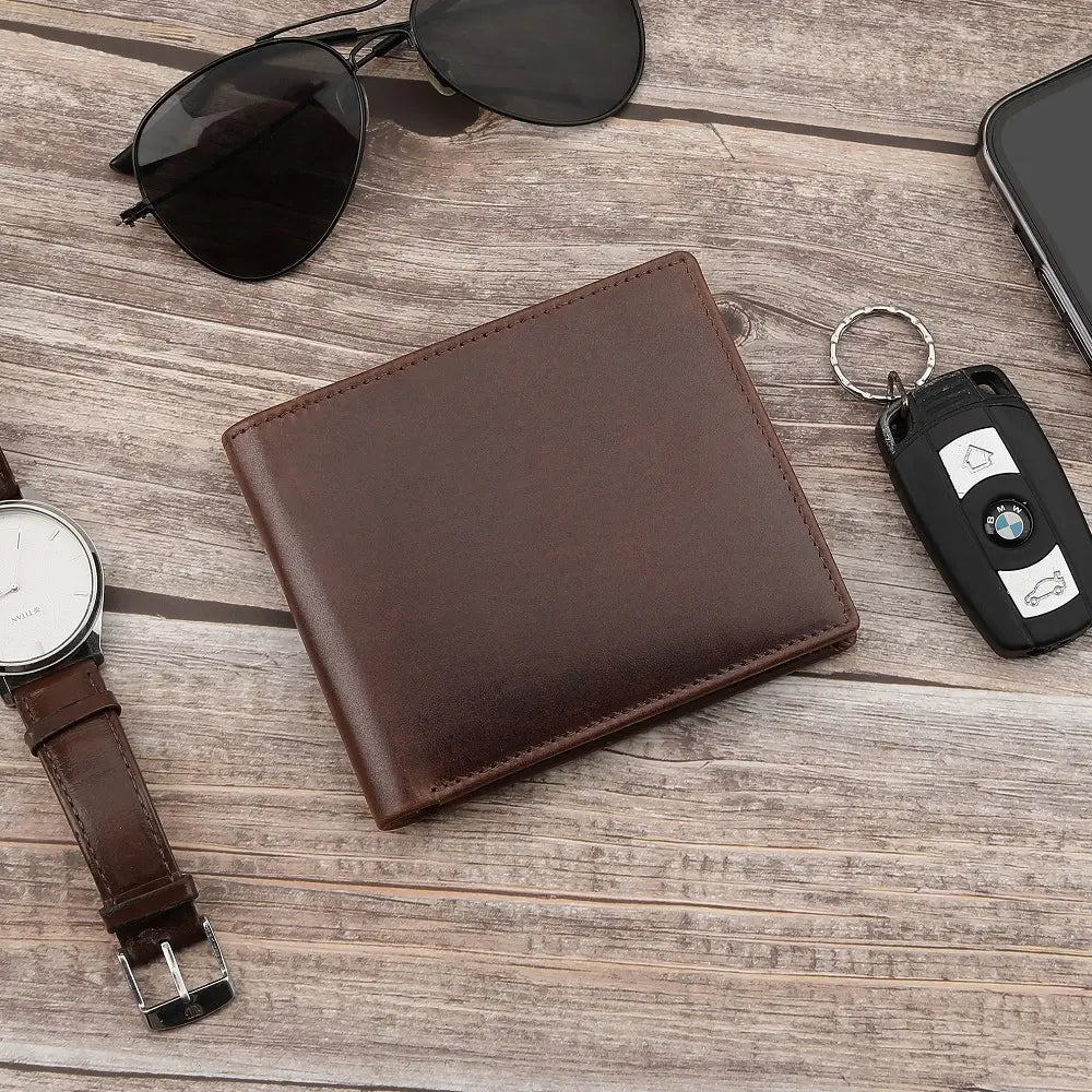 Brown  leather wallet, glasses, watch, phone, and car key fob on a white wooden surface.