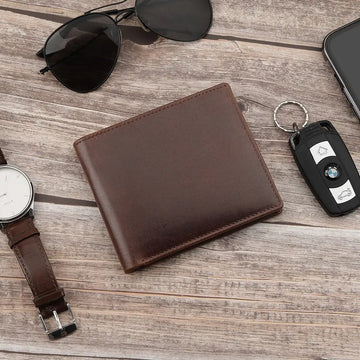 Brown  leather wallet, glasses, watch, phone, and car key fob on a white wooden surface.