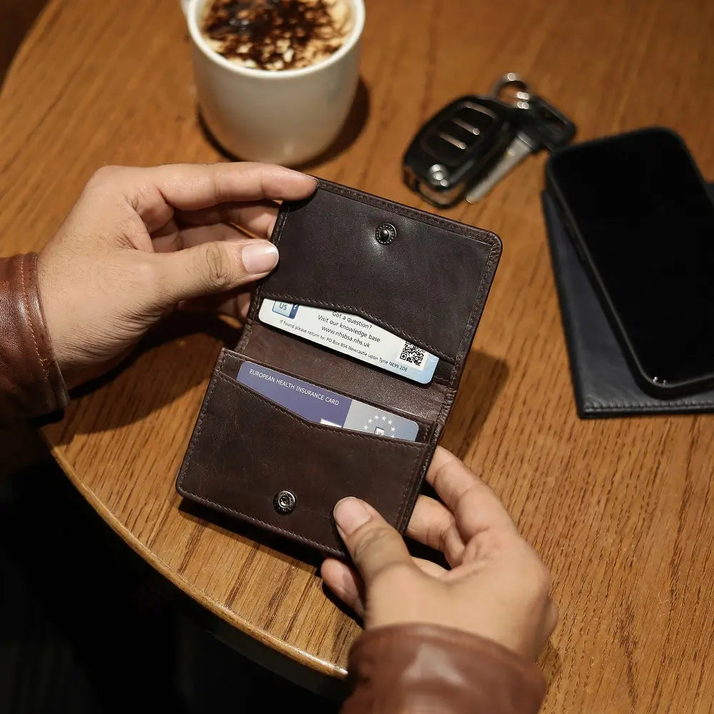 Brown leather Mayfair 2511 credit cardholder being used on a wooden café table beside a coffee cup and phone.