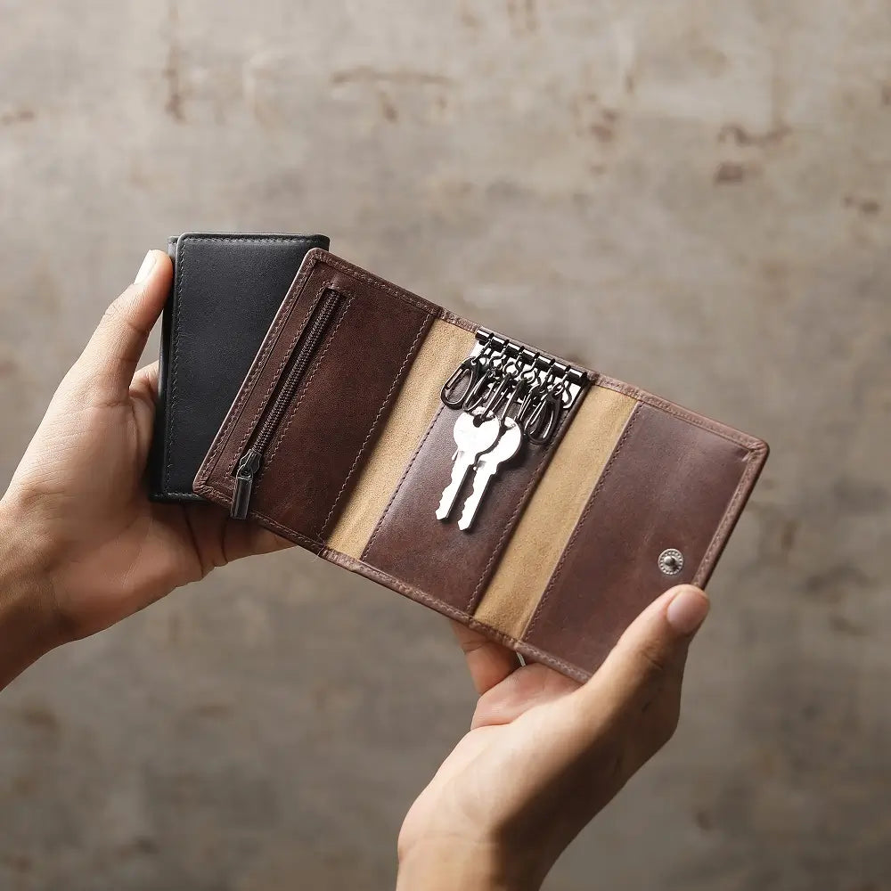 Brown leather wallet with key holder held by a hand against a neutral background
