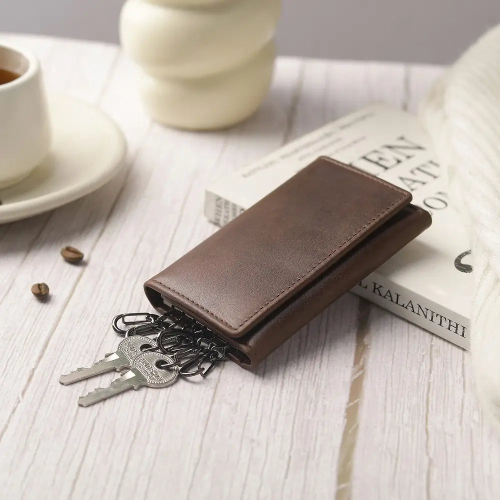 Brown leather wallet with keys on a wooden surface with a cup and saucer in the background.