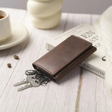 Brown leather wallet with keys on a wooden surface with a cup and saucer in the background.