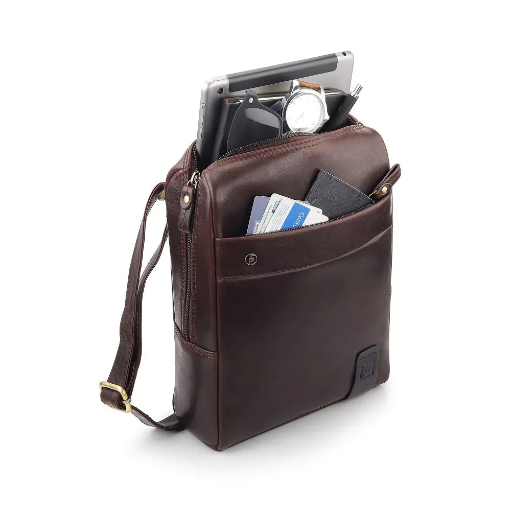 Brown leather messenger bag with items inside on a white background
