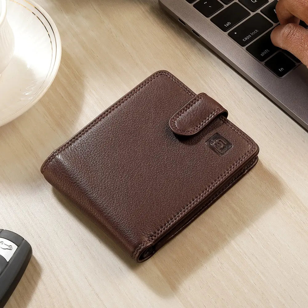 Brown leather wallet on a wooden desk with a laptop and glass of water in the background