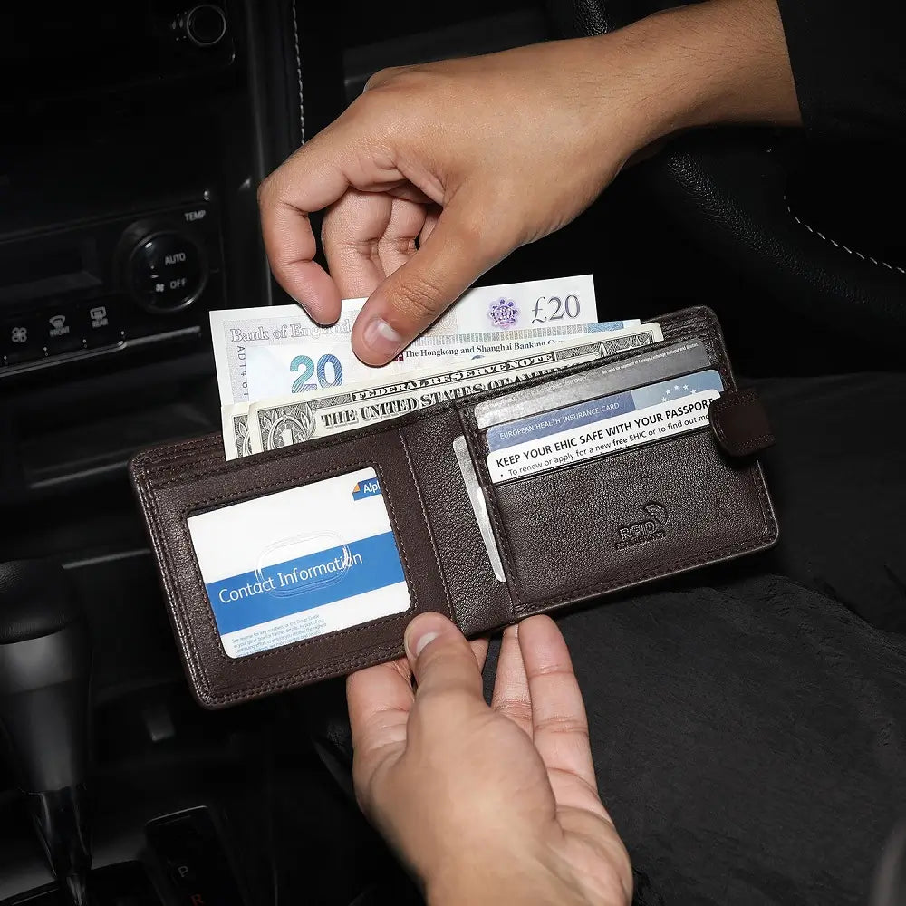 Person holding a brown leather wallet with cards and money in a car interior.