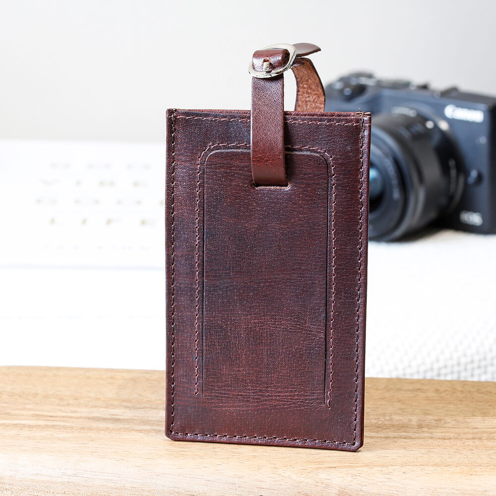 Brown leather luggage tag with a camera in the background on a wooden surface.