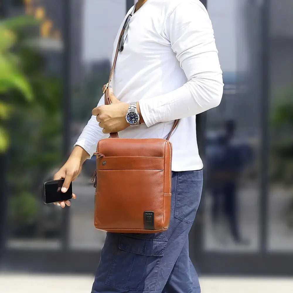 Person holding a tan leather messenger  bag and a smartphone with a blurred background