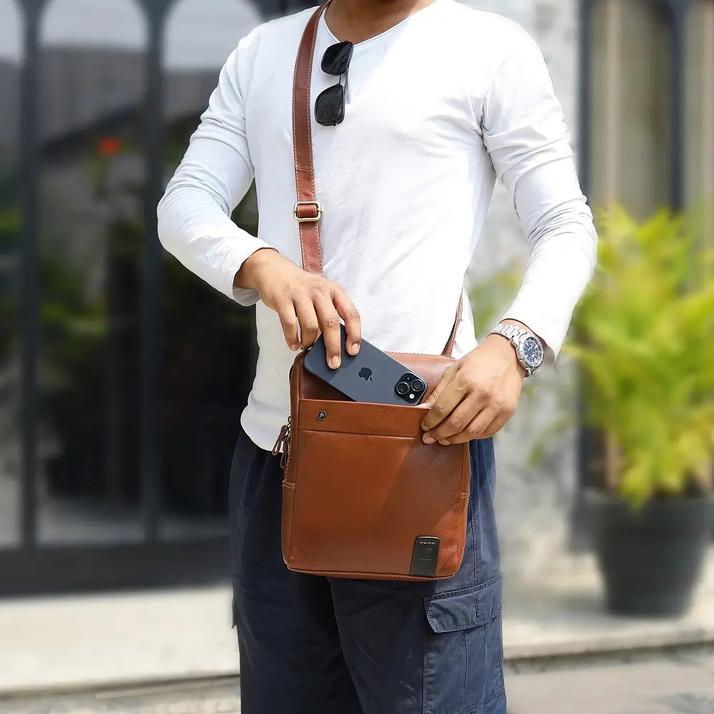 Person holding a tan leather messenger bag outdoors