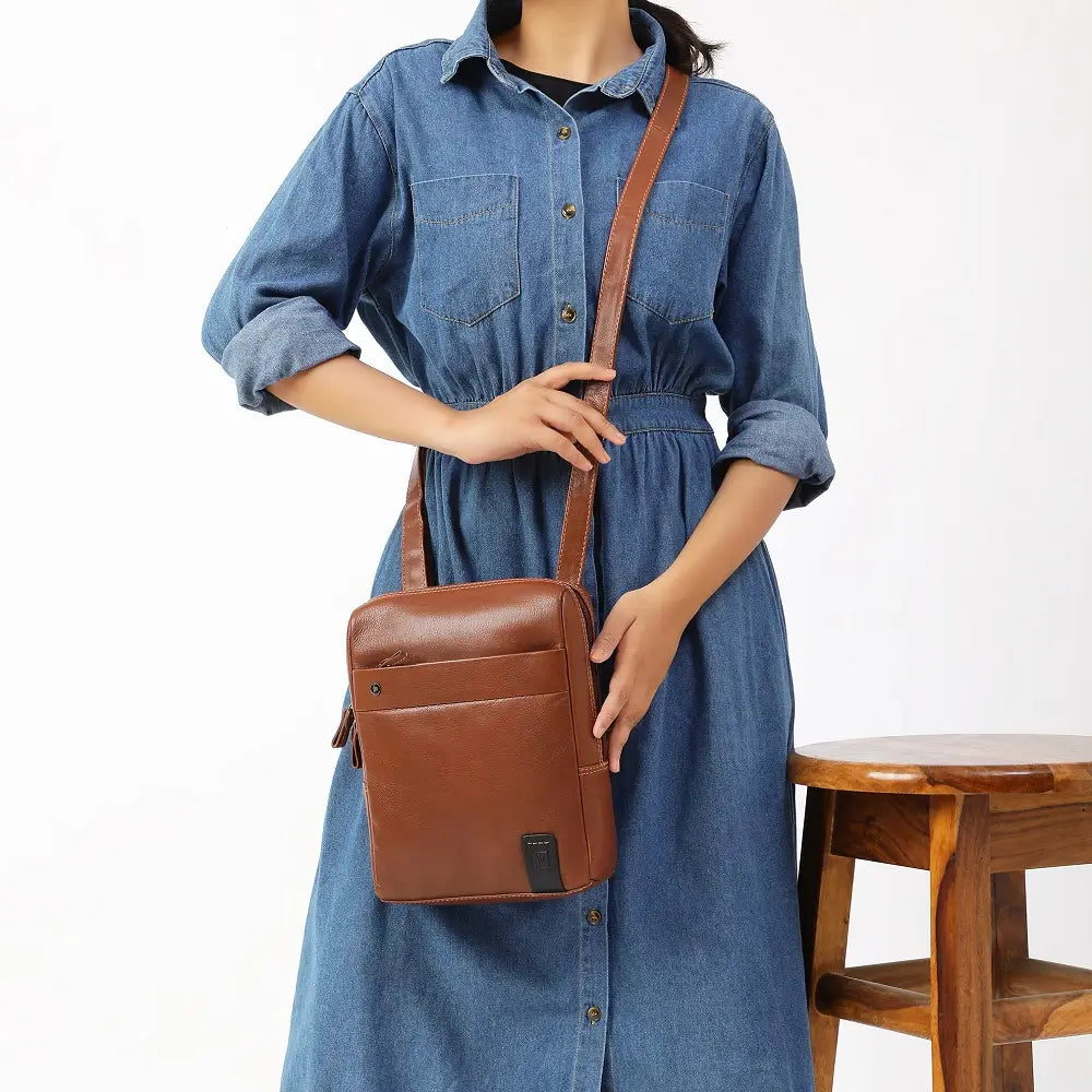 Person wearing a blue dress holding a tan messenger bag on a white background