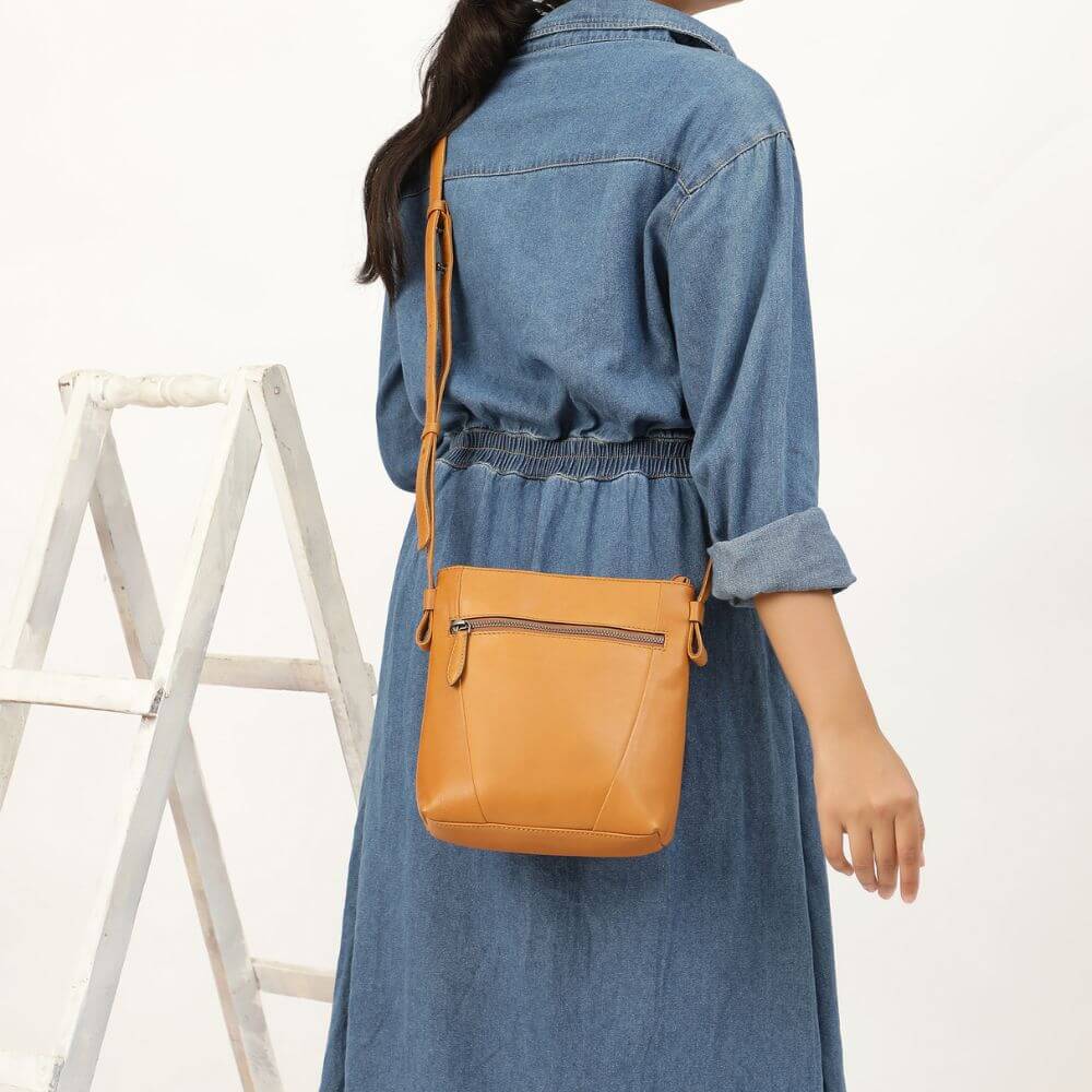 Person wearing a brown coat holding a black crossbody bag in a minimalistic setting with a plant.