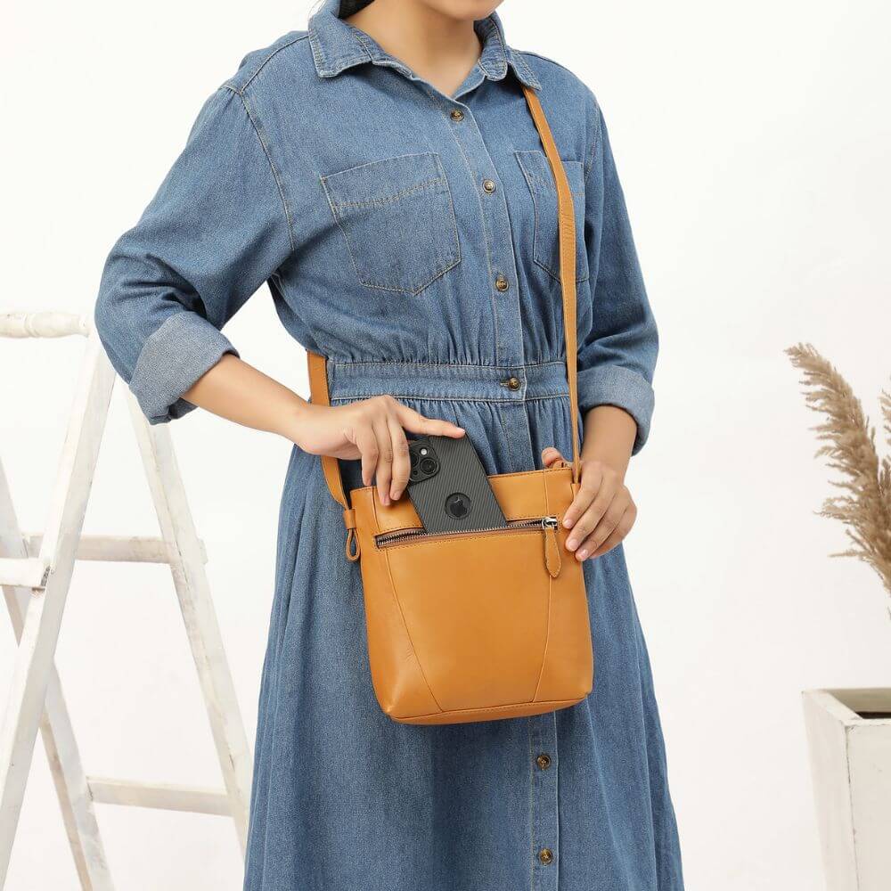 Person wearing a blue dress holding a tan crossbody bag with a white background