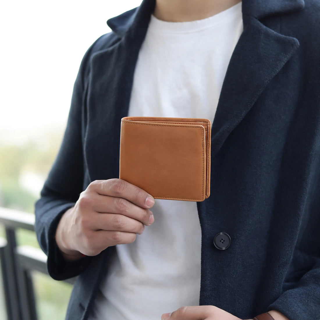 Person holding a cognac leather wallet with a blurred background