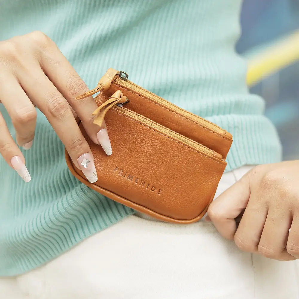 Cognac leather wallet with 'PRIMEHIDE' branding held by a person against a blurred background.