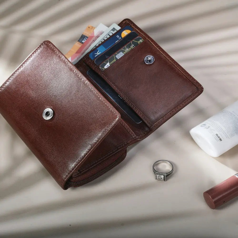 Cognac leather wallet with cards on a light surface with a bottle and lip gloss.