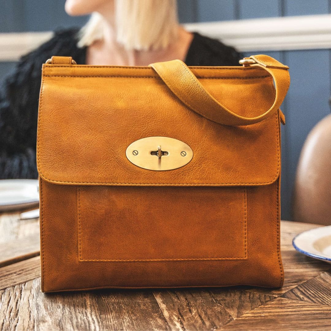 a woman is wearing a large yellow leather handbag in a crossbody style. The handbag has a long leather strap with brass buckle adjusters