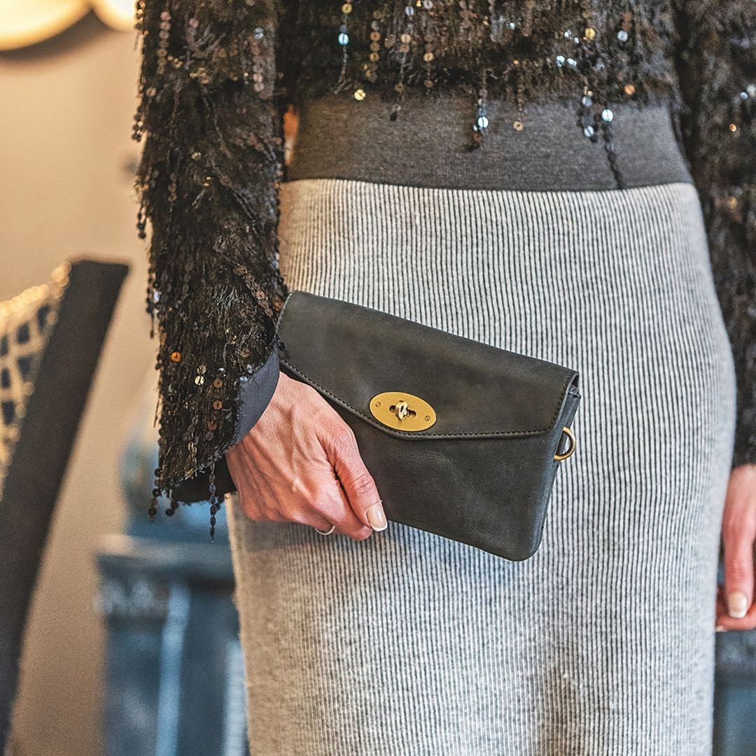 a woman is wearing a black leather jacket with a yellow leather crossbody bag. the bag has a centre brass coloured twist lock